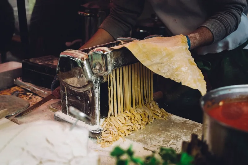 Fresh pasta sheets being rolled through a hand-crank pasta machine