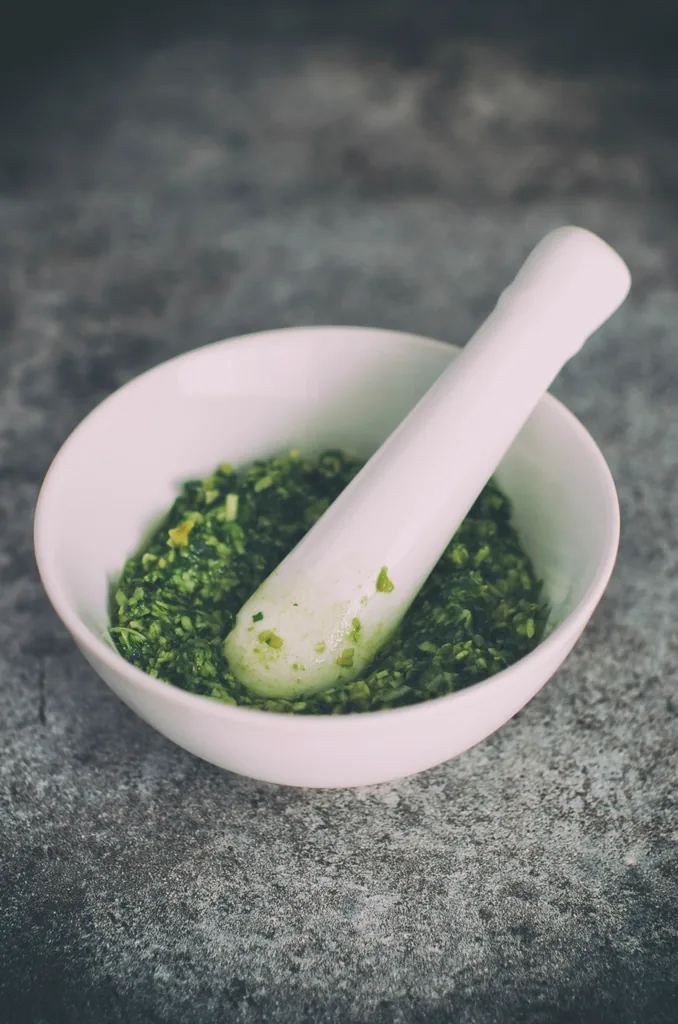 A stone mortar and pestle with freshly ground green herbs