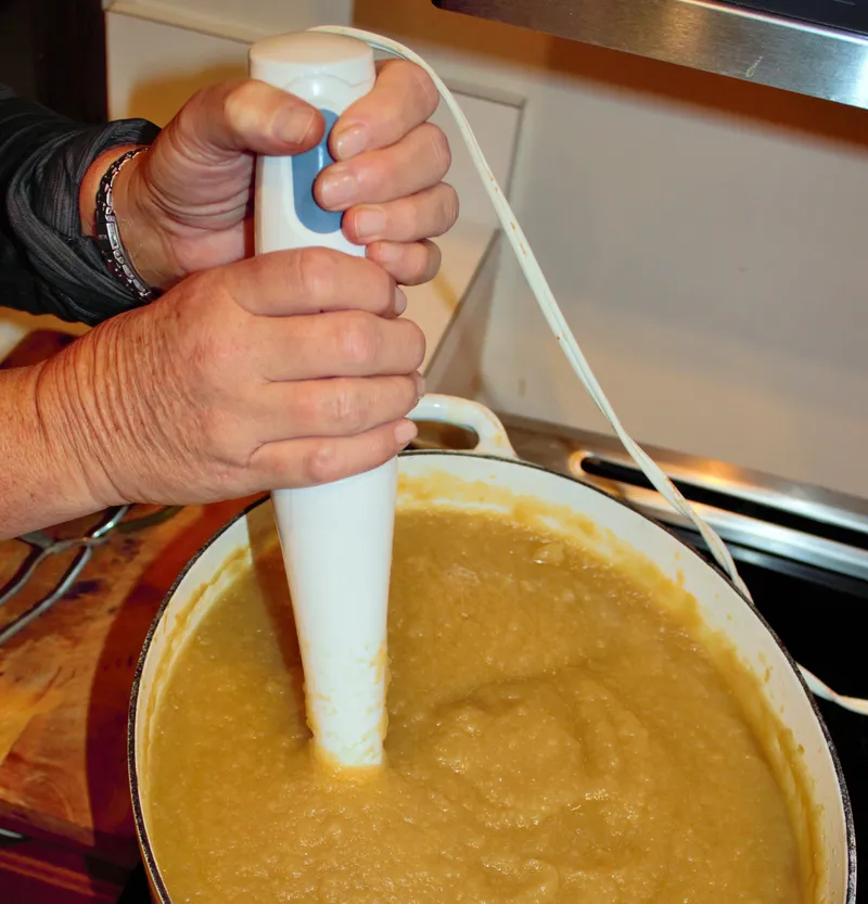 An immersion blender pureeing soup in a pot