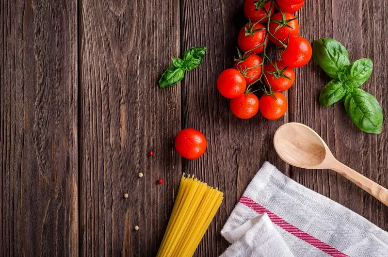 Flat lay of tomatoes, basil, dried pasta and a wooden spoon on a rustic table