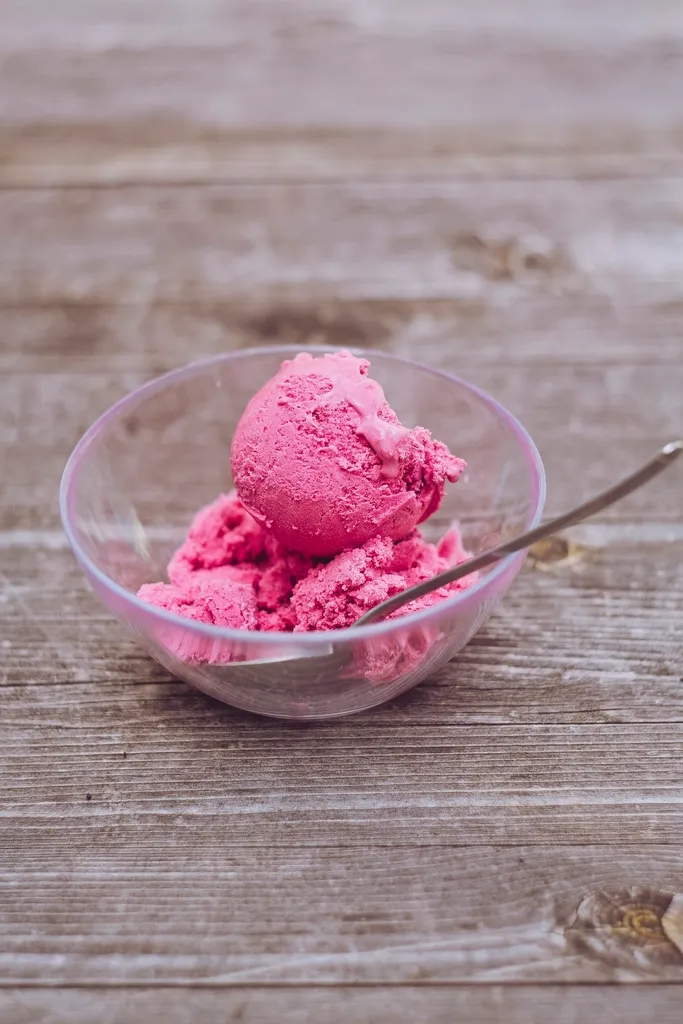 A glass bowl of pink berry ice cream with a spoon